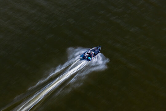 Aerial view of a fast fishing motor boat creating a white wake on dark water, Poland.