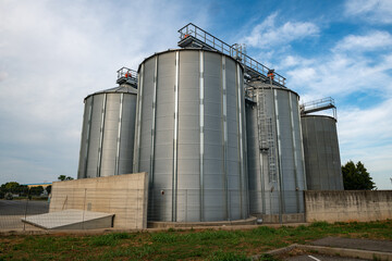 Grain storage silos at agricultural facility, metal cereal silos for wheat and corn, modern farming infrastructure, agribusiness logistics, food supply chain, harvest storage, industrial agriculture. © rikstock