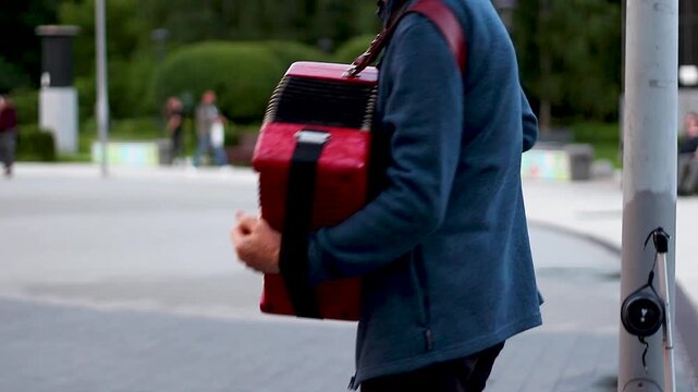 Musician carrying a red accordion through a busy public park