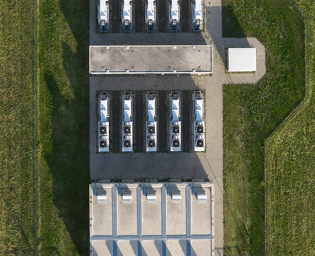 Aerial view of BESS Battery energy storage system with rows of industrial battery containers and cooling units on a paved site in green fields Uckermark, Brandenburg, Germany.