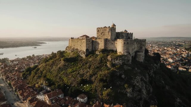 Majestic Castle Perched on Hilltop Overlooking River and Town at Sunset.