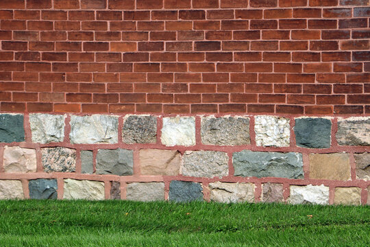 Red brick wall above historic rustic fieldstone foundation and green lawn