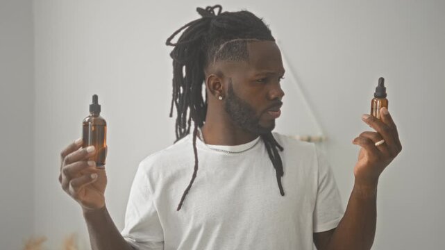 Man holding amber dropper bottles in both hands inspecting one bottle with a squint in a studio; contemplative grooming.