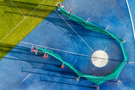 Aerial view of a hammer throw circle with a protective green net on a blue athletic track surface in Poland.