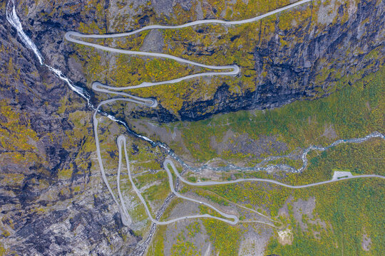 Aerial view of the Trollstigen mountain road with its sharp hairpin bends, steep rocky cliffs, and a winding river in Andalsnes, More og Romsdal, Norway.