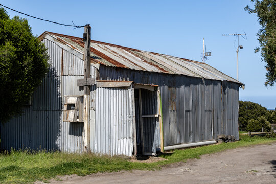 Rustic corrugated iron coastal shed with rusted metal roof and wooden utility pole&nbsp;a dirt road in&nbsp;Australia. Vernacular architecture, countryside, rural heritage concepts.