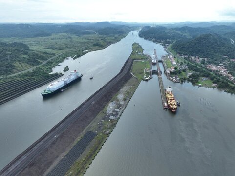 Aerial view of the Panama Canal with large cargo ships navigating through the locks surrounded by lush green hills in Panama City, Panama Province, Panama.