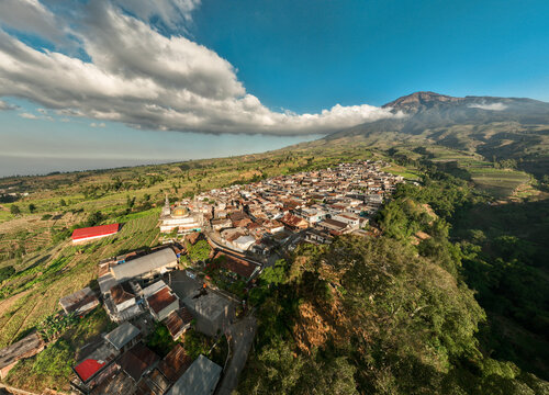 Aerial view of Kruwisan village nestled on the slopes of Mount Sindoro with terraced fields, a mosque with a golden dome, and lush green landscape in Kledung, Central Java, Indonesia.