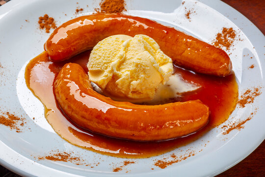 Caramelized bananas served with a scoop of vanilla ice cream and cinnamon powder on a white plate.