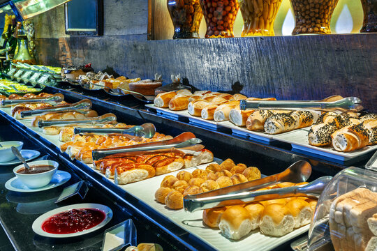 Luxury hotel breakfast buffet featuring a wide variety of fresh breads, pastries, and sweet jams displayed on an elegant counter with serving tongs.