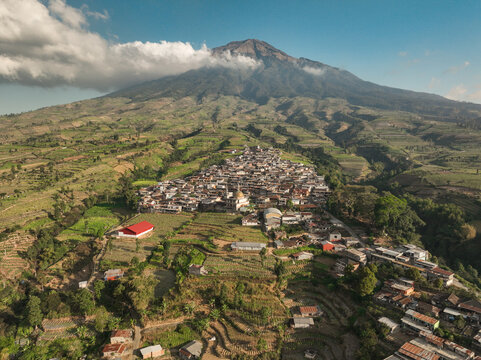 Aerial view of Kruwisan village nestled on the slopes of Mount Sindoro, surrounded by lush terraced agricultural fields and vibrant greenery in Kledung, Central Java, Indonesia.