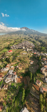Aerial view of Kruwisan village nestled in the terraced agricultural landscape near Mount Sindoro with lush green fields and traditional houses in Kledung, Central Java, Indonesia.