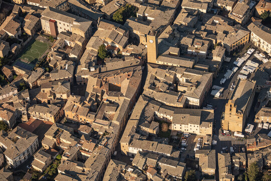 Aerial view of the historic center of Orvieto, featuring the Torre del Moro clock tower, dense terracotta rooftops, narrow stone streets, and a small sports court in Orvieto, Umbria, Italy.