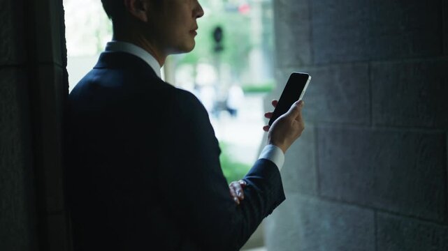 Backlit Japanese businessman checking his phone at a building entrance