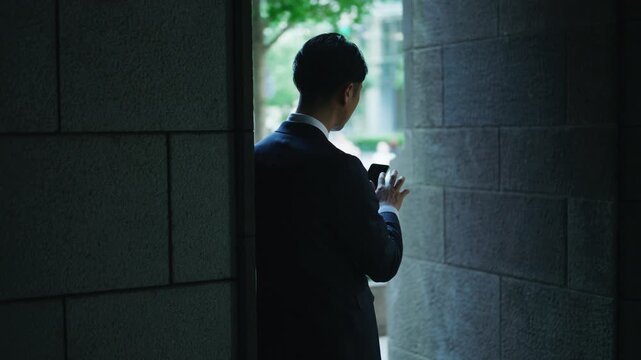 Silhouette of a businessman using a smartphone beside a stone column