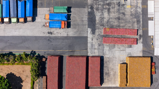 Aerial view of a logistics yard featuring trucks with colorful tarps and organized stacks of wooden pallets in Salatiga, Central Java, Indonesia.
