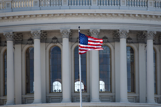 US flag on Capitol with dome architecture. Capitol with American flag near landmark. American flag near Capitol as patriotic symbol. Capitol with American flag for government background.