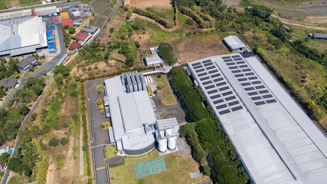 Aerial view of a large industrial facility featuring a warehouse with solar panels on its roof, storage silos, and surrounding greenery in Salatiga, Central Java, Indonesia.
