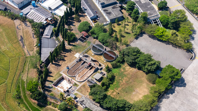 Aerial view of a wastewater treatment plant with circular sedimentation tanks and rectangular aeration basins near green trees and agricultural fields in Salatiga, Central Java, Indonesia.