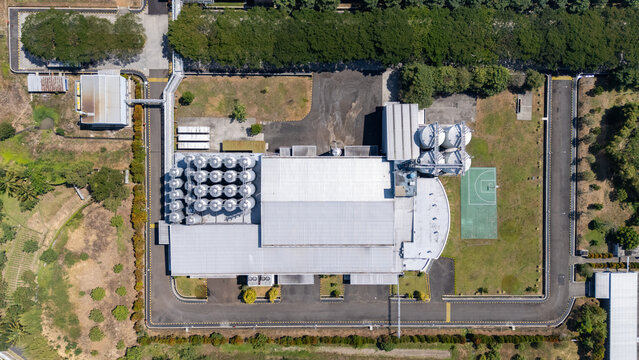 Aerial view of an industrial factory complex with metal storage silos, a large warehouse, and an adjacent basketball court surrounded by trees in Salatiga, Central Java, Indonesia.