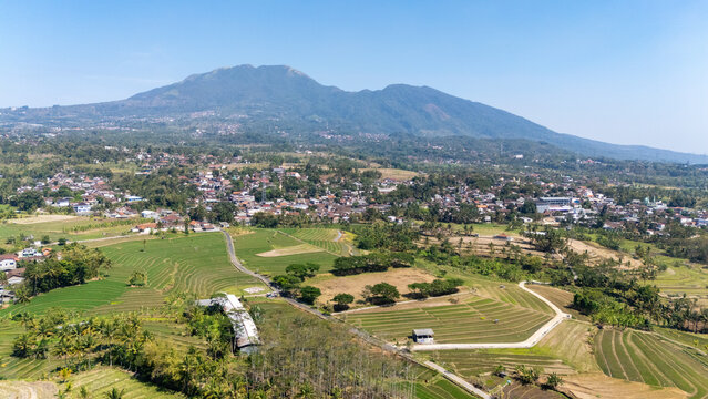 Aerial view of the town of Salatiga nestled among lush green rice terraces and tropical vegetation with a large mountain rising in the background in Salatiga, Central Java, Indonesia.