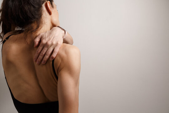Athletic woman herself hands massaging her upper back, trapezius muscles in pain, tension, soreness, recovery, posture, wellness. Selfcare after exercise with studio light copy space. Rear view