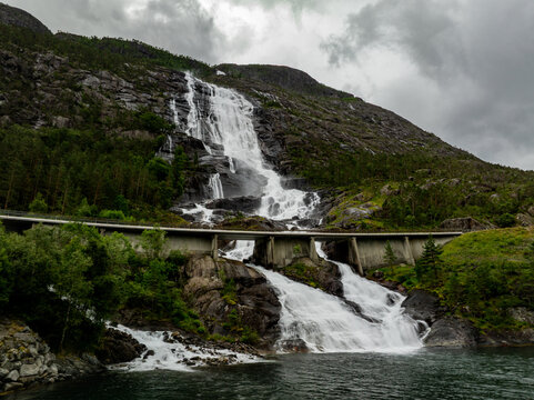 Aerial view of Langfoss waterfall cascading down a rocky mountain slope with a bridge crossing the stream and lush greenery in Fjaera, Vestland, Norway.