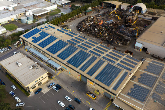 Aerial view of a large industrial warehouse covered with rooftop solar panel arrays beside a metal recycling facility in Sydney, New South Wales, Australia.