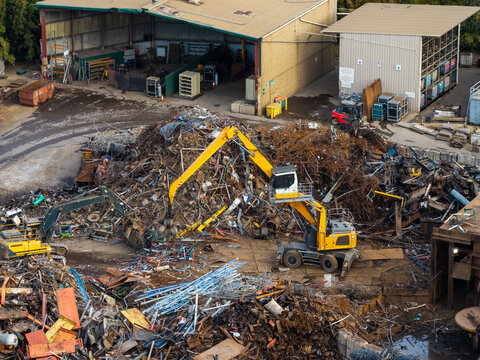 Aerial view of a scrap metal sorting operation with an industrial material handler sorting through piles of discarded metal at a recycling facility in Sydney, New South Wales, Australia.