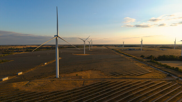 Aerial view of wind and solar renewable energy park at sunset with rows of photovoltaic panels and large wind turbines across the rural landscape Chelveston, England, United Kingdom.