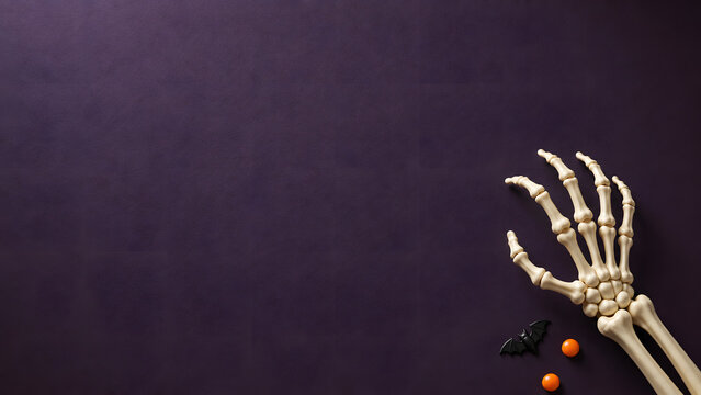 Spooky Halloween skeleton hand with bats on purple background, creepy skeleton arm party copy space background, holiday composition