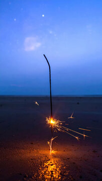 Firework sparkler on dark beach beneath blue twilight sky