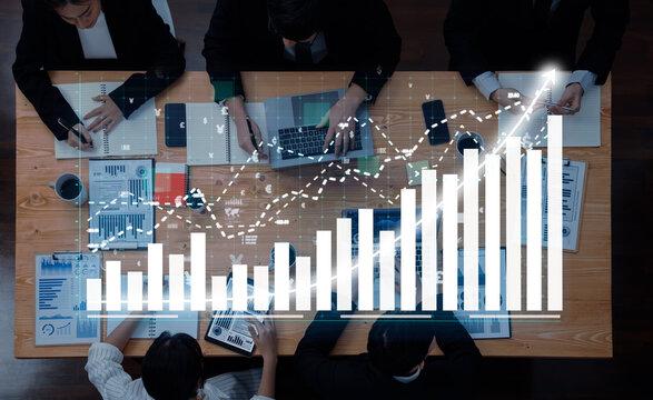 A dynamic scene of business professionals collaborating over financial charts and graphs on laptops at a wooden table, focusing on growth and strategic planning. Axiom