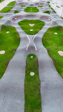 Aerial view of a modern pump track featuring asphalt curves and grassy patches in Riga, Latvia.