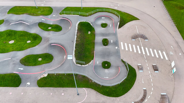 Aerial view of a modern asphalt pumptrack with curves and green grass areas in a park in Riga, Latvia.