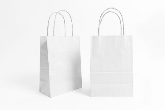 Studio shot of two blank white paper bags from different angles. Eco-friendly packaging mockup for retail, branding, and commercial use, isolated on white background.