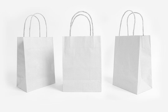 Studio shot of three blank white paper bags shown from different angles. Eco-friendly packaging mockup for retail, branding, and commercial use, isolated on white background.