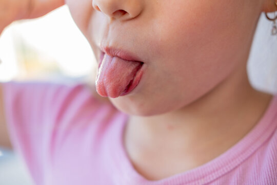 Teasing or joking gesture used kids express silliness, closeup little girl sticking tongue out, playful naughty expression, pink shirt, macro shot mouth and nose, funny childhood emotion, skin texture