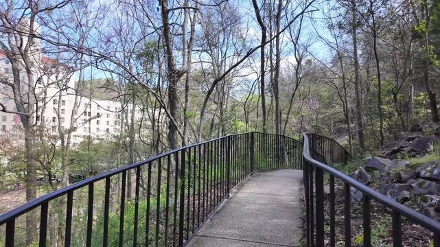 Curved paved path with metal railings through wooded area.