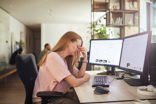 Stressed woman with headache at computer in modern office