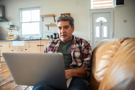 Middle-aged man using laptop on couch in home kitchen