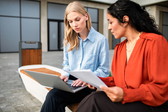 Two businesswomen reviewing documents on laptop outside office