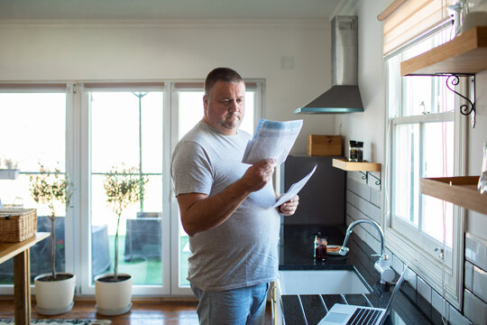 Concerned man reviewing utility bills in home kitchen