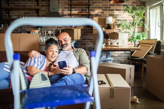Middle-aged couple checking phone while moving into new home