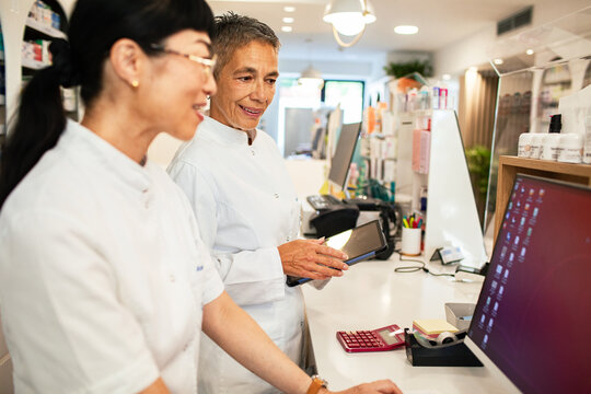 Two pharmacists using tablet and computer in modern pharmacy