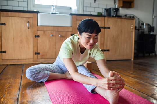 Smiling woman stretching on yoga mat in home kitchen