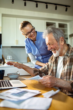 Caregiver assisting happy senior man with bills at kitchen table