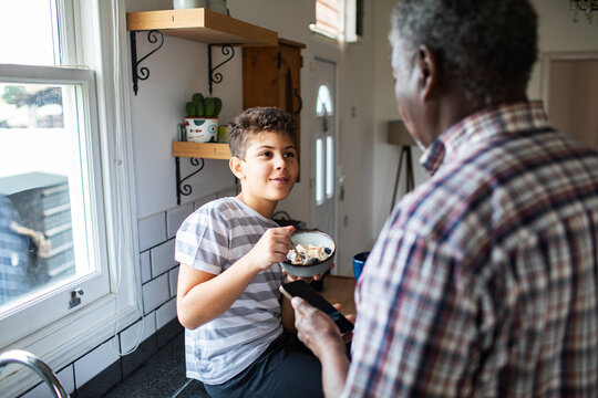 Teen boy eating breakfast with parent in home kitchen