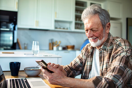 Smiling senior man using smartphone at kitchen table