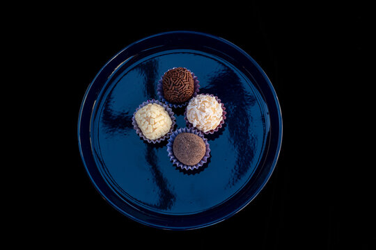 Brigadeiros, Brazilian truffles, on a dark blue plate with a black background. The dark plate of small, round Brazilian desserts is used at birthday parties and weddings. The balls are flavored.